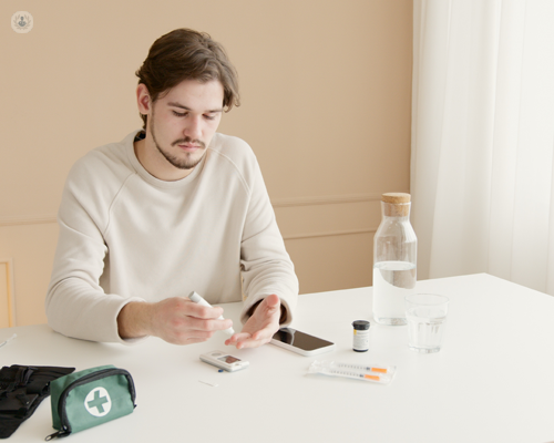 Young man taking his blood sugar levels at a table with the bag and other equipment he needs for diabetes managment